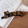 Détail d'une pince à cheveux chat en écaille de tortue faite à la main sur un livre - Pince Banane Chat Strass / Ambre