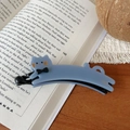 Détail de la pince banane chat bleu clair avec marquage doré sur fond de livre - Pince Banane Chat Strass / Bleu Brume