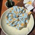 Light blue scrunchie with citrus fruit pattern displayed on a ceramic dish in sunlight - Orange Orchard Sea Salt Blue Scrunchie