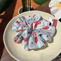 Light blue satin scrunchie with strawberry pattern and a small red brand tag - Small Tomato Orchard Blue Scrunchie