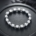 Geometrisches silbernes Metallarmband mit quadratischen Perlen auf Holztablett - Silber