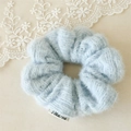 Detail of soft blue plush knitted scrunchie with white brand label and textile texture - Blue