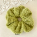 Close-up of a soft light green plush hair scrunchie with a sewn-on white brand label - Green