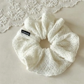 Detailed macro view of cream lace scrunchie with a handmade woven label detail - White