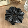 Détail du chouchou en satin noir avec motif argenté sur fond de table en bois rustique - Noir