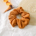 Detail of ginger yellow linen hair scrunchie with rich folds on a straw mat background - Orange