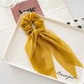 Detail view of ginger yellow chiffon scrunchie with long flowing ribbons in a tray - Yellow