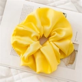 Macro shot of an oversized bright yellow satin scrunchie with silky pleated texture - Yellow