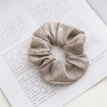 Close-up of champagne gold metallic hair scrunchie with pleated texture on a book - Gray
