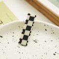 Close-up of black and white checkered hair claw clip with scalloped edges on ceramic tray - Wave Style