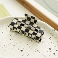 Detailed top view of a classic black and white checkered hair claw clip on a ceramic plate - Rectangle