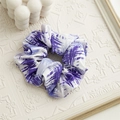 Dettaglio scrunchie in raso viola con stampa geometrica astratta su sfondo crema testurizzato - Tie-dye