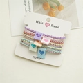 Dettaglio di 5 elastici per capelli color macaron con trama intrecciata e etichette - Stile Intrecciato