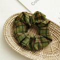 Close-up of a dark green plaid fabric scrunchie placed on a woven tray with soft lighting - Green Plaid