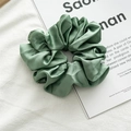 Detail of oversized sage green satin scrunchie with smooth texture on a magazine - Thin Style / Army Green