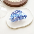 Detail view of transparent blue hair claw clip with floral patterns on white tray - Semicircle Blue