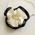 Vue détaillée du chouchou crème avec bordure noire et lettrage CHANGE blanc élégant - Blanc