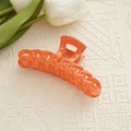 Détail d'une pince à cheveux orange translucide avec charnière dorée et design en chaîne - Orange