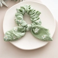 Close-up of light green scrunchie with daisy pattern and bow on a ceramic tray - Daisy Ears Green