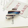 Detail shot of a large striped acetate hair claw clip on a minimalist magazine background - Gradient Blue