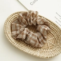 Brown checkered fabric scrunchie with soft pleats on a minimalist woven tray background - Coffee Plaid