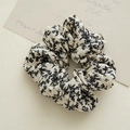Dettaglio macro dell'elastico scrunchie in tessuto beige con motivi floreali neri - Bianco
