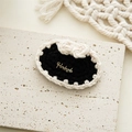 Detail of a handmade black knitted hair clip featuring a cream bow and gold metal tag - Black Base with White Bowtie