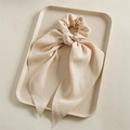 Detalle de coletero beige claro con lazo y cintas largas sobre bandeja texturizada - Cinta Beige