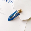 Dettaglio di un fermaglio per capelli in resina blu con clip in metallo dorato e testo - Blu scuro
