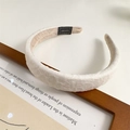 Dettaglio del cerchietto plissettato beige con etichetta Hand Made su sfondo di legno - Bianco Sporco
