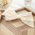 Close-up of cream bow hair clip with daisy embroidery on a wooden tray with decor - Cream White Embroidered