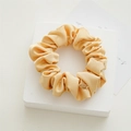 Detailed macro of smooth warm yellow satin scrunchie featuring a premium gold metal tag - Yellow
