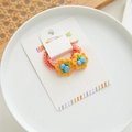 Detail of orange elastic hair ties with yellow floral charms on a handmade card - Blueberry