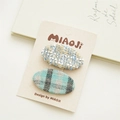 Close-up of two fabric hair clips featuring blue tweed and plaid textures on a display card - Grey Green Plaid