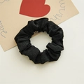 Close-up of black fabric hair scrunchie with soft pleated texture on decorative card - Black