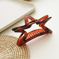 Detail view of a matte star-shaped claw clip with tortoiseshell pattern and metal spring - Matte Amber