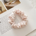 Detail of soft pink satin scrunchie with pleated texture on a magazine background - Pink
