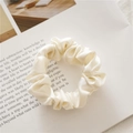 Close-up of cream white silk scrunchie with soft satin luster on a magazine background - Milky White