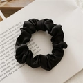 Close-up of black satin scrunchie with silk luster on a white aesthetic book - Black