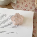 Translucent pink camellia flower hair claw clip on an open book in a warm home setting - Flower Style Jelly Pink