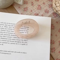 Detailed close-up of a pink resin geometric hair claw clip on vintage book and floral fabric - Round Style Jelly Pink
