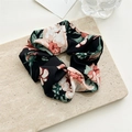 Primer plano de coletero con estampado floral sobre placa de piedra beige y luz suave - A Negro
