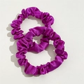 Detail view of two dark purple satin silk scrunchies with elegant pleated texture - Purple