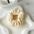 Macro detail of cream pleated satin hair scrunchie on a white textured decorative tray - Milky Yellow