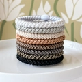 Detailed view of seven colorful braided hair ties stacked on a white ceramic plate - Coffee Black Palette