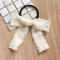 Detail of cream bow scrunchie with pleated edges on textured mother-of-pearl and wood surface - Hair Tie White Pleated Bow