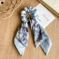 Detalle de coletero floral azul claro con cinta de satén sobre mesa de madera - Doble Azul