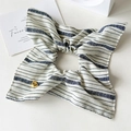 Dettaglio dello scrunchie a fiocco a righe blu e bianche con ciondolo a cuore dorato Lucky - Elastico Bianco a Righe