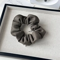 Detailed view of a dark taupe suede scrunchie with a white woven label on a display tray - Retro Suede Grey