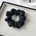 Close-up of black pleated faux leather scrunchie with brand label on a display tray - Retro Suede Black